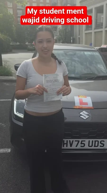 Woman holding a driving test certificate in front of an L-plate car, celebrating passing her exam